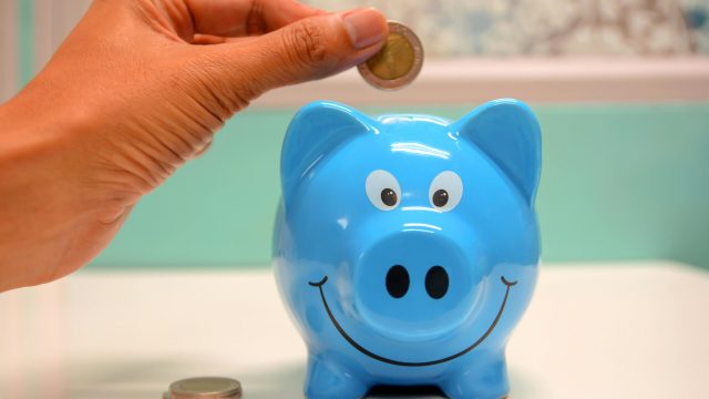 pexels-photo-1602726-1602726 Hand inserting a coin into a blue piggy bank for savings and money management.